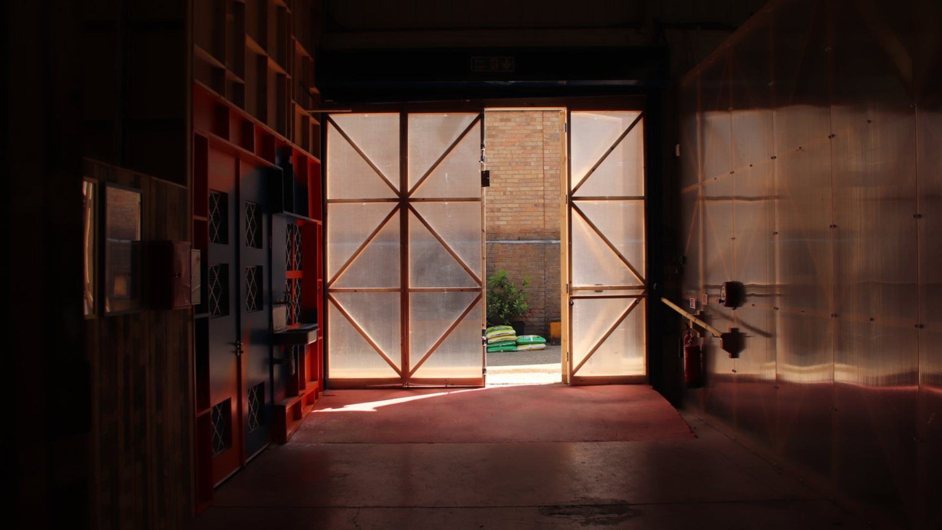 Image shows a large door made of polycarbonate showing an alley way with greenery outside.