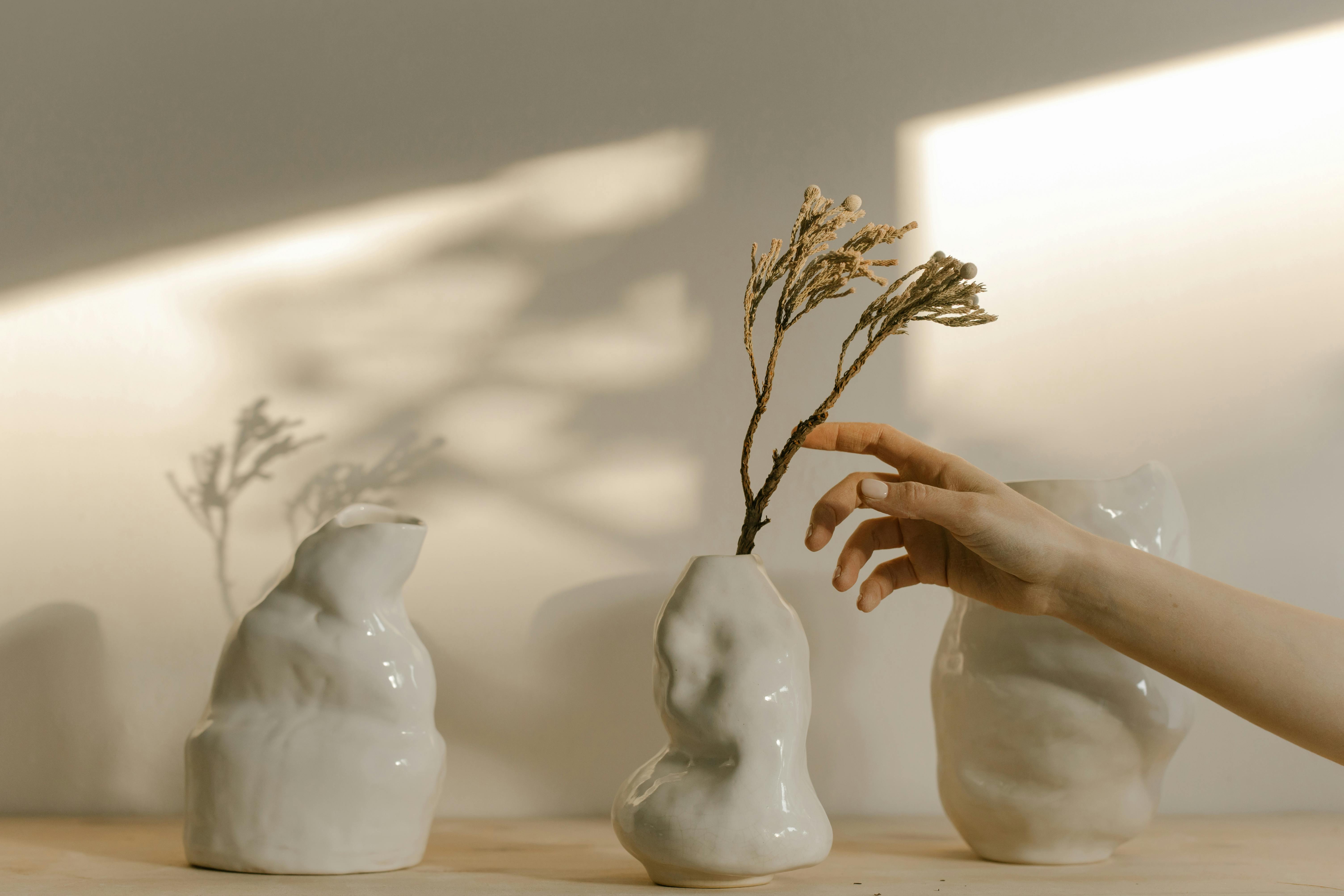Three handmade white ceramic vases and a hand reaching for some flowers
