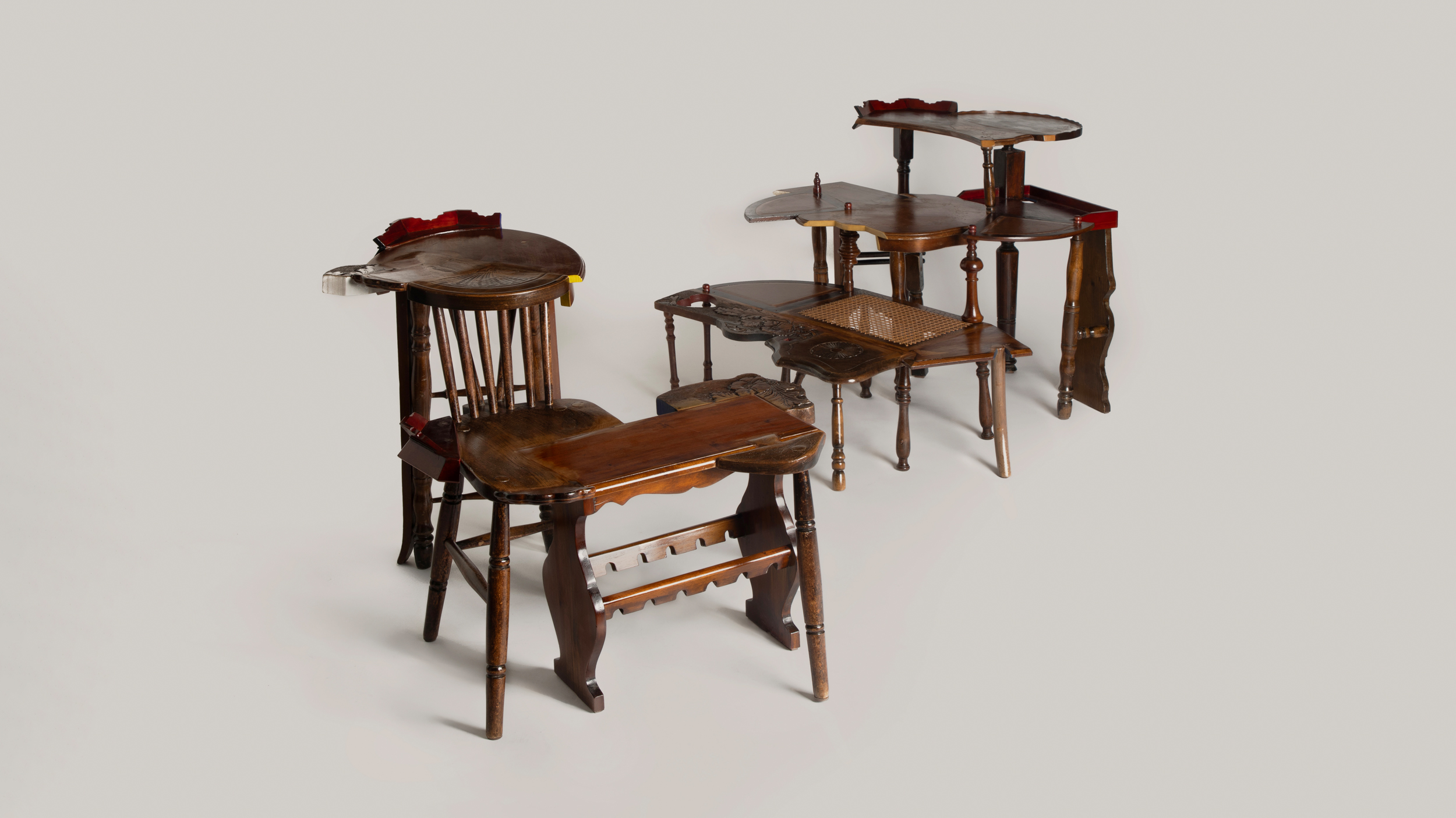Two sculptural furniture pieces made from assembled vintage wooden chairs and tables, forming abstract, hybrid designs.